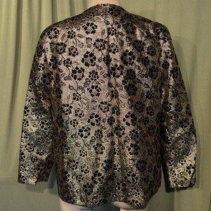 May include: A black and gold brocade jacket with a floral pattern. The jacket has long sleeves and a V-neck.