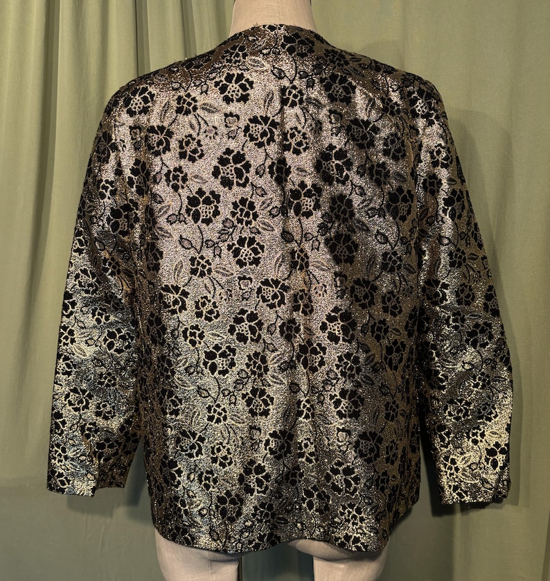 May include: A black and gold brocade jacket with a floral pattern. The jacket has long sleeves and a V-neck.