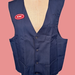May include: A navy blue vest with a V-neck, button closure, and two front pockets. An "ACME" patch is sewn on the left chest. The vest is displayed on a mannequin.