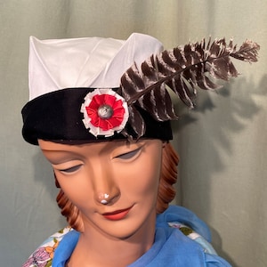 May include: A white hat with a black band and a red and white flower accent. A brown feather is attached to the side of the hat.