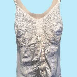 Op de afbeelding: Ivoor vintage korset met kanten details. Het korset heeft een ritssluiting aan de voorkant, verstelbare bandjes en jarretelgordel bevestigingen. De bodice is gemaakt van een satijnachtig materiaal, met kanten accenten op de buste en het bovenste gedeelte.