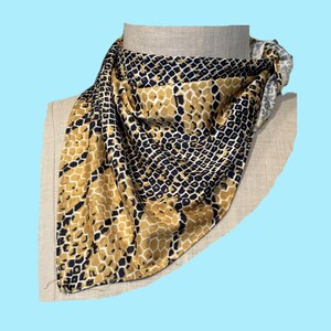 May include: A square scarf with a snakeskin pattern in shades of gold, black, and white. The scarf is draped over a mannequin head, showcasing its design and texture. The fabric appears to be silky.