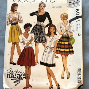 May include: McCall's sewing pattern for a skirt, size 12. The pattern shows four different skirt styles: a yellow skirt, a plaid skirt, a white skirt with a black trim, and a red skirt. The pattern is titled "Fashion Basics" and includes the text "Tops not included, Hauts non compris".
