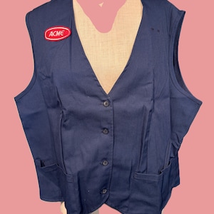 May include: A navy blue vest with a V-neck, button closure, and two front pockets. An "ACME" patch is on the upper left chest. The vest is made of a durable fabric and is likely part of a uniform.