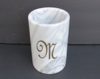 May include: White marble utensil holder with a gold "M" monogram.