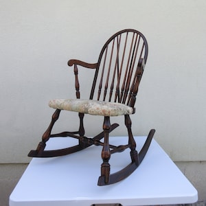May include: A wooden rocking chair with a floral patterned cushion. The chair has a spindle back and turned legs.