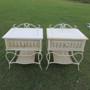May include: Two white wicker end tables with a drawer and a lower shelf. The tables have a white painted metal frame with a decorative scroll design.