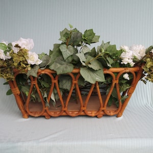 May include: A brown wicker planter filled with white flowers and green leafy plants.