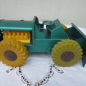 May include: A vintage toy bulldozer with a green metal body and yellow plastic wheels. The bulldozer has a yellow plastic engine and a metal steering wheel.