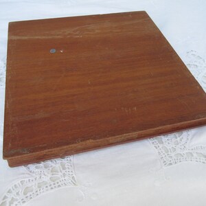 May include: A wooden square tray with a smooth, brown surface. The tray has a slightly raised edge.