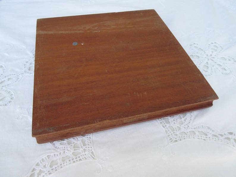 May include: A wooden square tray with a smooth, brown surface. The tray has a slightly raised edge.