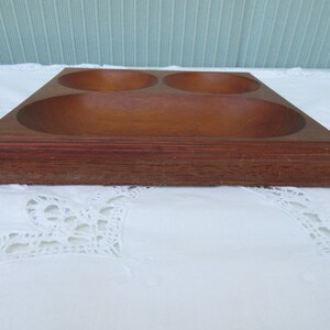 May include: A wooden serving tray with three separate bowls. The tray is made of dark brown wood and has a smooth finish.