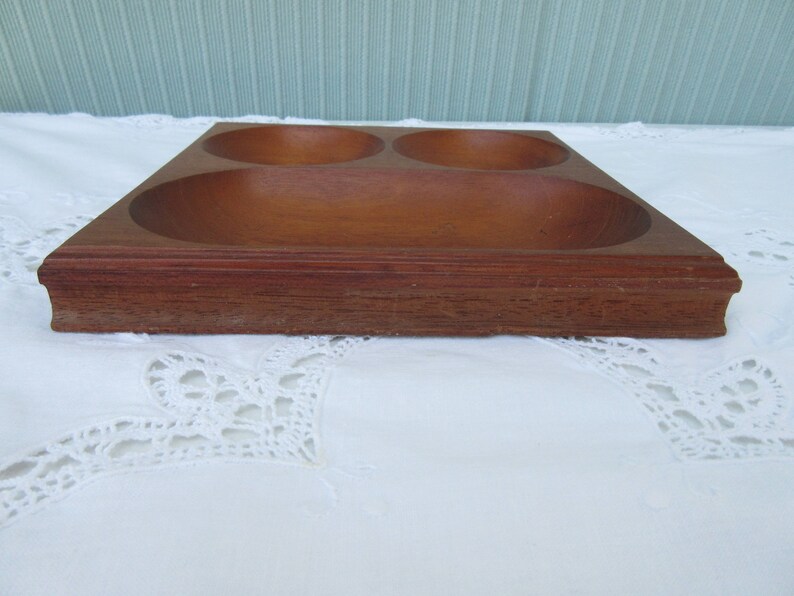 May include: A wooden serving tray with three separate bowls. The tray is made of dark brown wood and has a smooth finish.