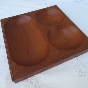 May include: A wooden serving tray with three separate bowls. The tray is made of dark brown wood and has a smooth finish. The bowls are also made of wood and have a rounded shape.