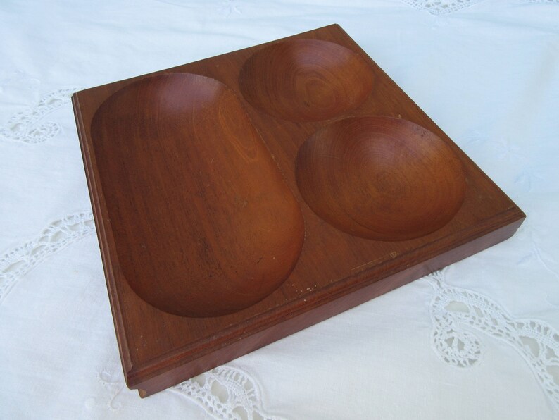 May include: A wooden serving tray with three separate bowls. The tray is made of dark brown wood and has a smooth finish. The bowls are also made of wood and have a rounded shape.