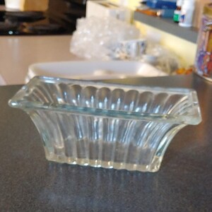 May include: A clear glass dish with a rectangular shape and a ribbed design. The dish is empty and sitting on a gray surface.