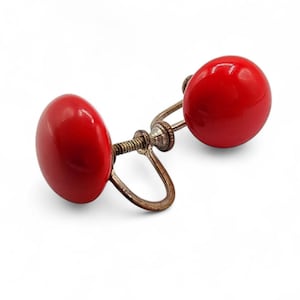May include: A pair of vintage screw-back earrings. Each earring has a vibrant red, glossy, round cabochon. The metal components have a tarnished, antique appearance, with a screw mechanism. These earrings are a classic accessory.