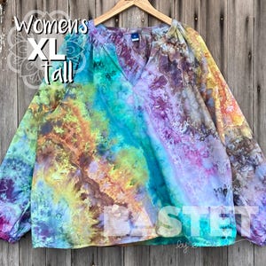 May include: A multi-coloured tie-dye shirt with long sleeves and a V-neck. The shirt features shades of purple, blue, yellow, and orange. The text "XL tall" is visible. The word "BASTET" is at the bottom of the shirt.