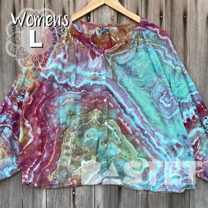 May include: A long-sleeved button-down shirt with a tie-dye pattern in shades of blue, purple, and green. The shirt has a relaxed fit and is labelled "Women's L". The sleeves have decorative cutouts.
