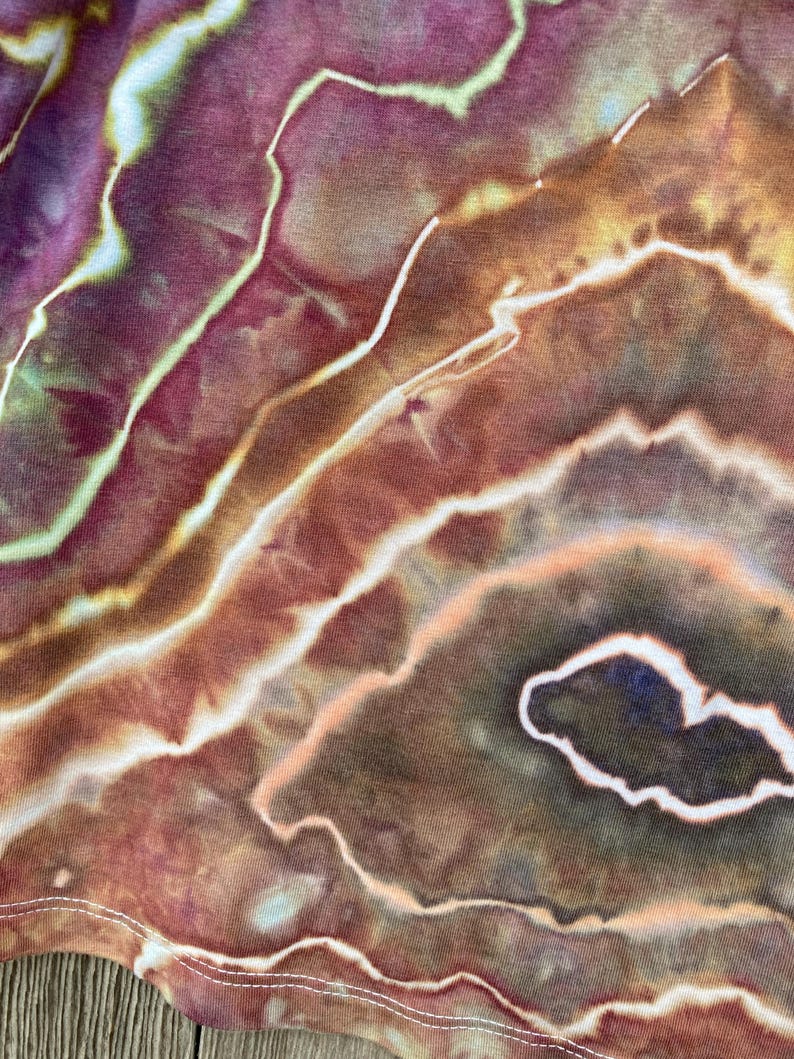 May include: Close-up of a tie-dye fabric with a swirling pattern of brown, orange, and white. The fabric has a soft, textured feel.