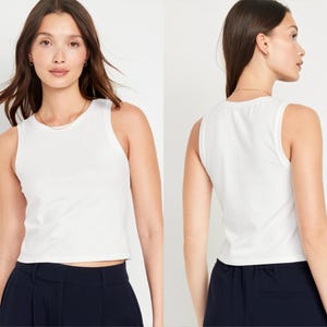 May include: White sleeveless cropped tank top with a scoop neck. The tank top is made of a soft, comfortable fabric and has a relaxed fit.