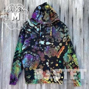 Pode incluir: Uma camisa de moletom com capuz preta com um padrão tie-dye em tons de verde, roxo e laranja. A camisa de moletom tem um tamanho unissex M.