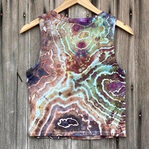 May include: A tie-dye tank top with a brown, green, and purple swirl pattern. The tank top is sleeveless and has a cropped length.