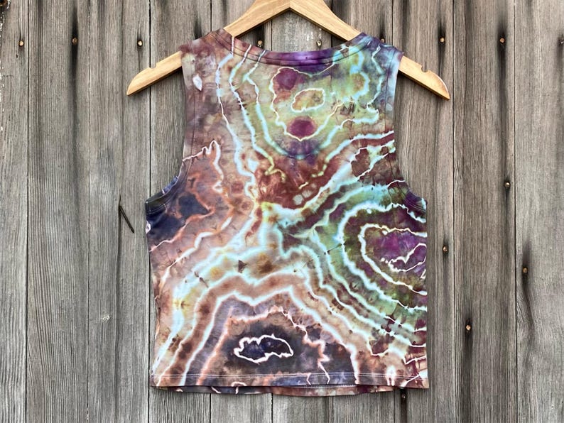 May include: A tie-dye tank top with a brown, green, and purple swirl pattern. The tank top is sleeveless and has a cropped length.