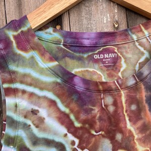 May include: A tie-dye tank top with a brown, green, and purple color scheme. The tank top has a scoop neck and a tag that reads "Old Navy" with the size "L" and "Made in Nicaragua".