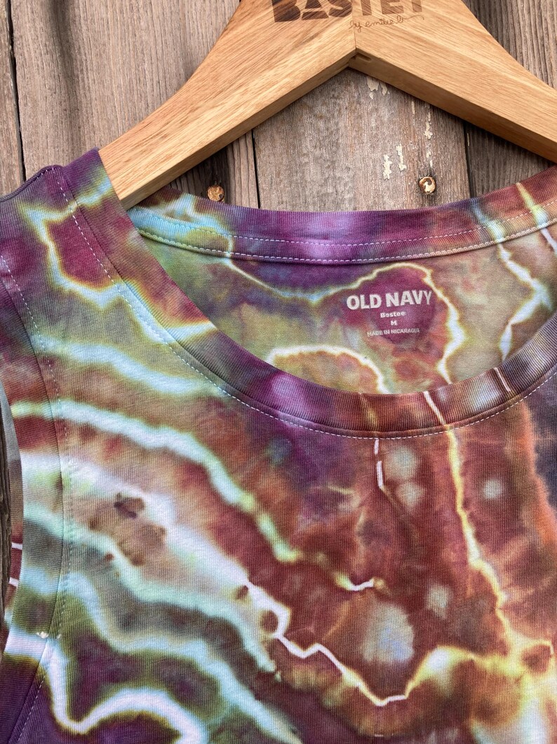 May include: A tie-dye tank top with a brown, green, and purple color scheme. The tank top has a scoop neck and a tag that reads "Old Navy" with the size "L" and "Made in Nicaragua".