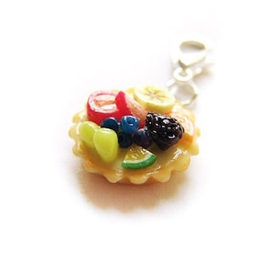 May include: A miniature fruit tart charm with a yellow crust, topped with red, green, and blue fruit, and a black berry.