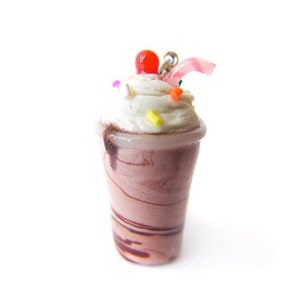May include: A miniature chocolate milkshake with whipped cream, a red cherry, and sprinkles in a clear plastic cup with a pink straw.