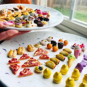K&ouml;nnte beinhalten: Eine Sammlung von Miniatur-Lebensmittel-Anh&auml;ngern, darunter Pizzast&uuml;cke, Tacos, Hotdogs, Eiswaffeln, Cupcakes, Donuts und vieles mehr. Die Anh&auml;nger sind aus Polymer Clay gefertigt und haben ein realistisches Aussehen.