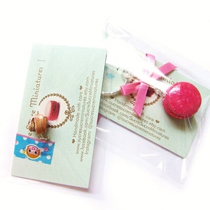 May include: A pair of pink and brown macaron charm earrings with silver hooks. The earrings are handmade and come with a card that says "Sucre Sucre Miniatures" and includes contact information for the shop.