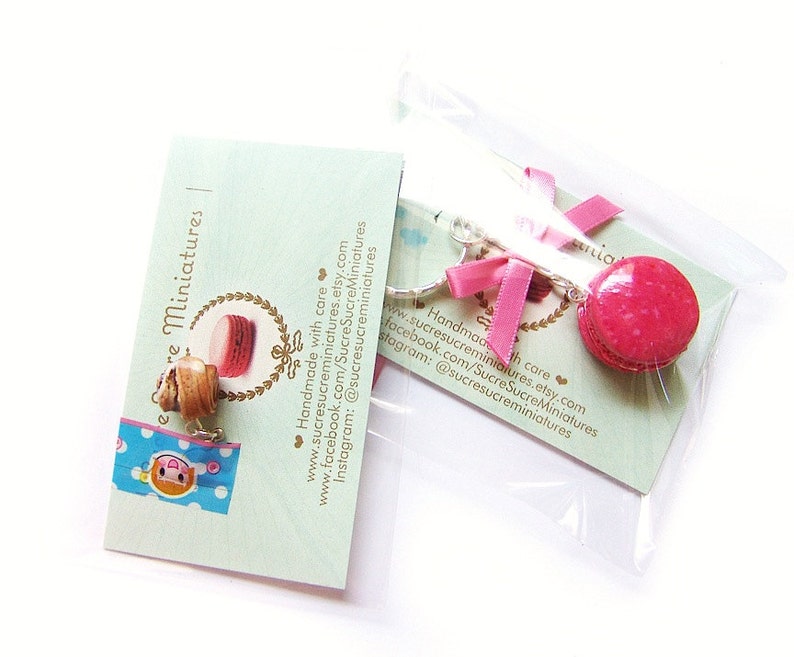 May include: A pair of pink and brown macaron charm earrings with silver hooks. The earrings are handmade and come with a card that says "Sucre Sucre Miniatures" and includes contact information for the shop.