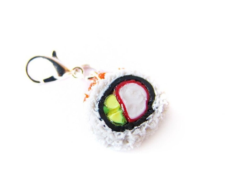 May include: A white, red, and green sushi roll charm with a silver lobster claw clasp. The sushi roll is made of polymer clay and is a realistic representation of a California roll.