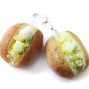 Könnte beinhalten: Zwei Miniatur-Backkartoffel-Ohrringe mit Belägen. Ein Ohrring hat einen weißen Klecks Sauerrahm, Frühlingszwiebeln und gewürfelten Käse. Der andere Ohrring hat einen gelben Klecks Butter und gewürfelten Käse.