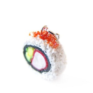 May include: A miniature sushi roll charm with a white rice exterior, black seaweed, and red and green fillings. The charm is topped with red tobiko (flying fish roe) and has a silver loop for hanging.