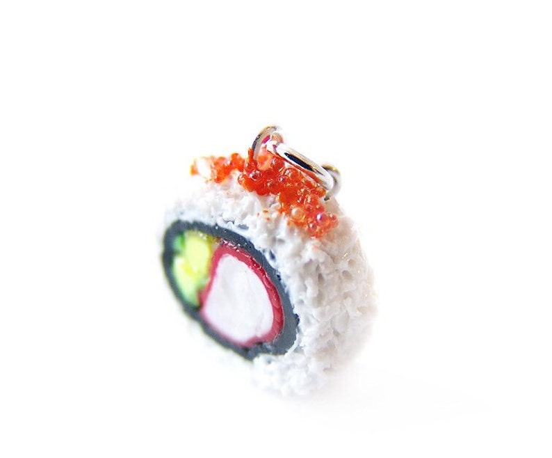 May include: A miniature sushi roll charm with a white rice exterior, black seaweed, and red and green fillings. The charm is topped with red tobiko (flying fish roe) and has a silver loop for hanging.