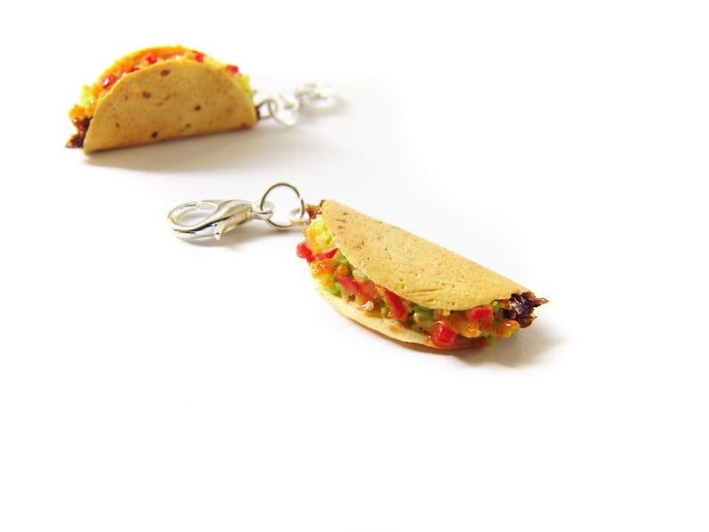 K&ouml;nnte beinhalten: Zwei Miniatur-Taco-Anh&auml;nger mit silbernen Verschl&uuml;ssen. Die Tacos sind mit Salat, Tomate und Fleisch gef&uuml;llt.