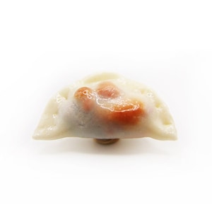 May include: A single, white, crescent-shaped dumpling with a brown filling. The dumpling is sitting on a white surface.