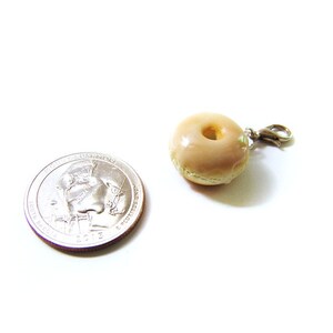 May include: A small, glazed donut charm with a silver clasp. The donut is about the size of a US quarter.