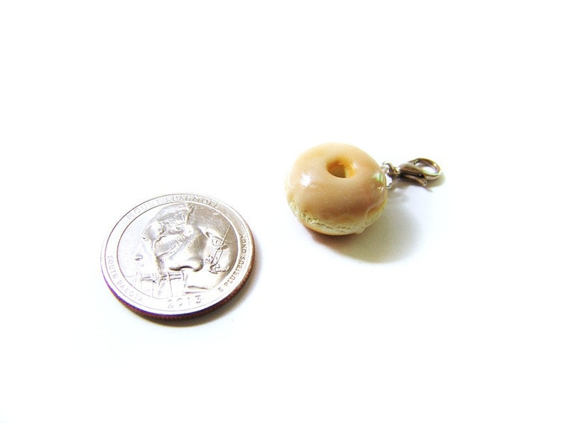 May include: A small, glazed donut charm with a silver clasp. The donut is about the size of a US quarter.