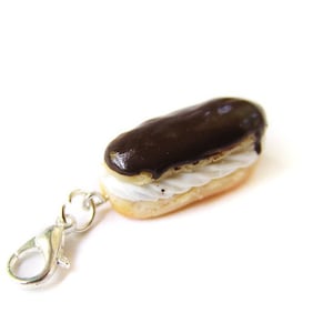 Könnte beinhalten: Ein silberner Anhänger in Form eines Schokoladeneclairs mit weißer Füllung. Der Anhänger hat einen Karabinerverschluss.