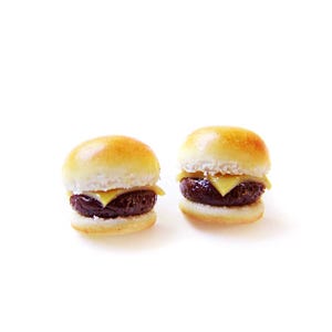 May include: Two miniature cheeseburgers with sesame seed buns, a beef patty, and a slice of cheese.