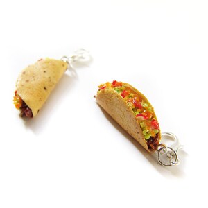 K&ouml;nnte beinhalten: Ein Paar silberne Taco-Ohrringe. Ein Ohrring zeigt einen Taco, gef&uuml;llt mit Guacamole, Tomaten und Zwiebeln. Der andere Ohrring zeigt einen einfachen Taco.