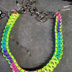 May include: A multi-colored paracord keychain with a silver chain and two silver clasps. The paracord is woven in a pattern with pink, green, blue, and yellow.