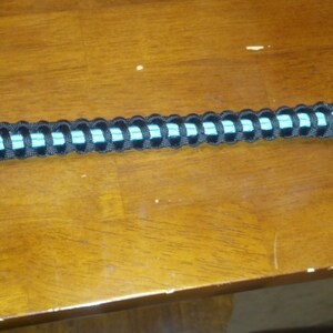 May include: A black and light blue paracord bracelet with a silver key ring attached.