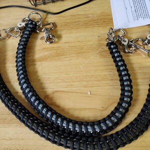 May include: Two black and gray paracord keychain lanyards with silver metal clasps and rings.