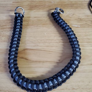 May include: A black and gray paracord leash with silver metal rings on each end.